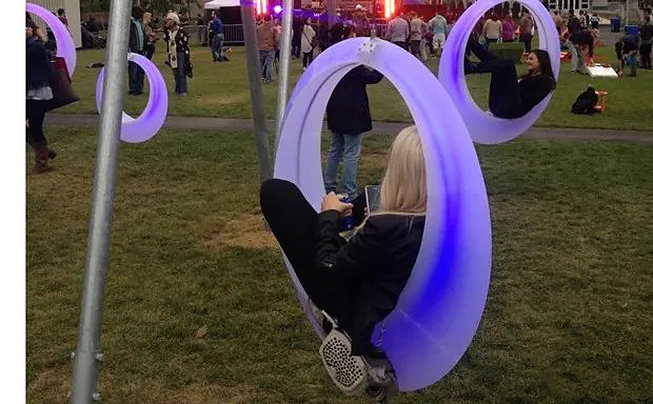 Illuminated swings on a lawn at dusk, with people sitting in them